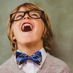 a young boy with blue bow-tie and glasses laughing with his head back