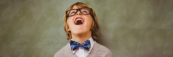 a young boy with blue bow-tie and glasses laughing with his head back