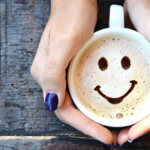 female hands holding coffee mug with smiling foam