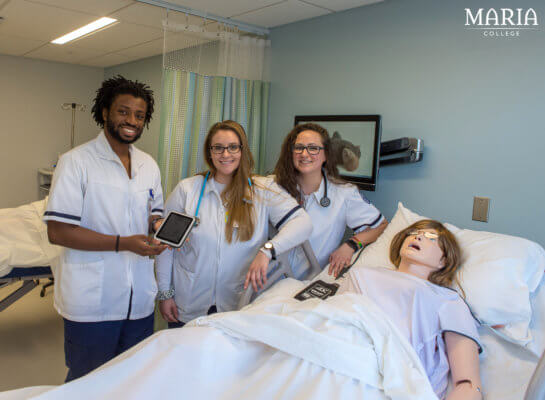 three nursing students in simulation lab next to manikin