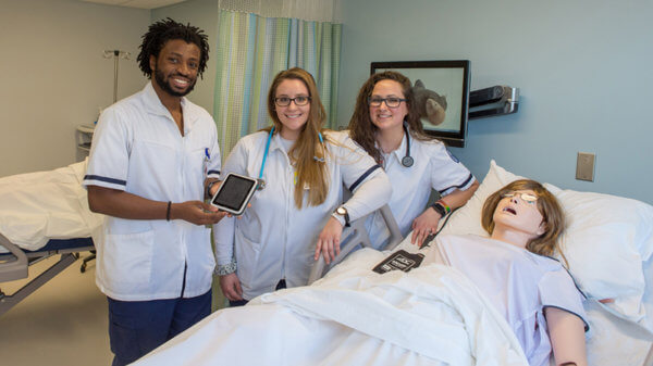 three nursing students in simulation lab next to manikin